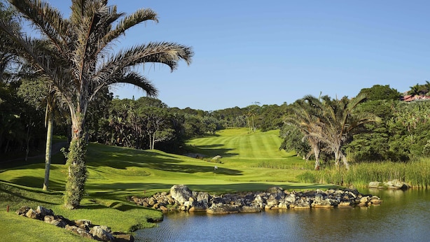 A golf course with a pond, palm trees, and a clear sky. - San Lameer Villa Rentals  2827 (Southbroom)