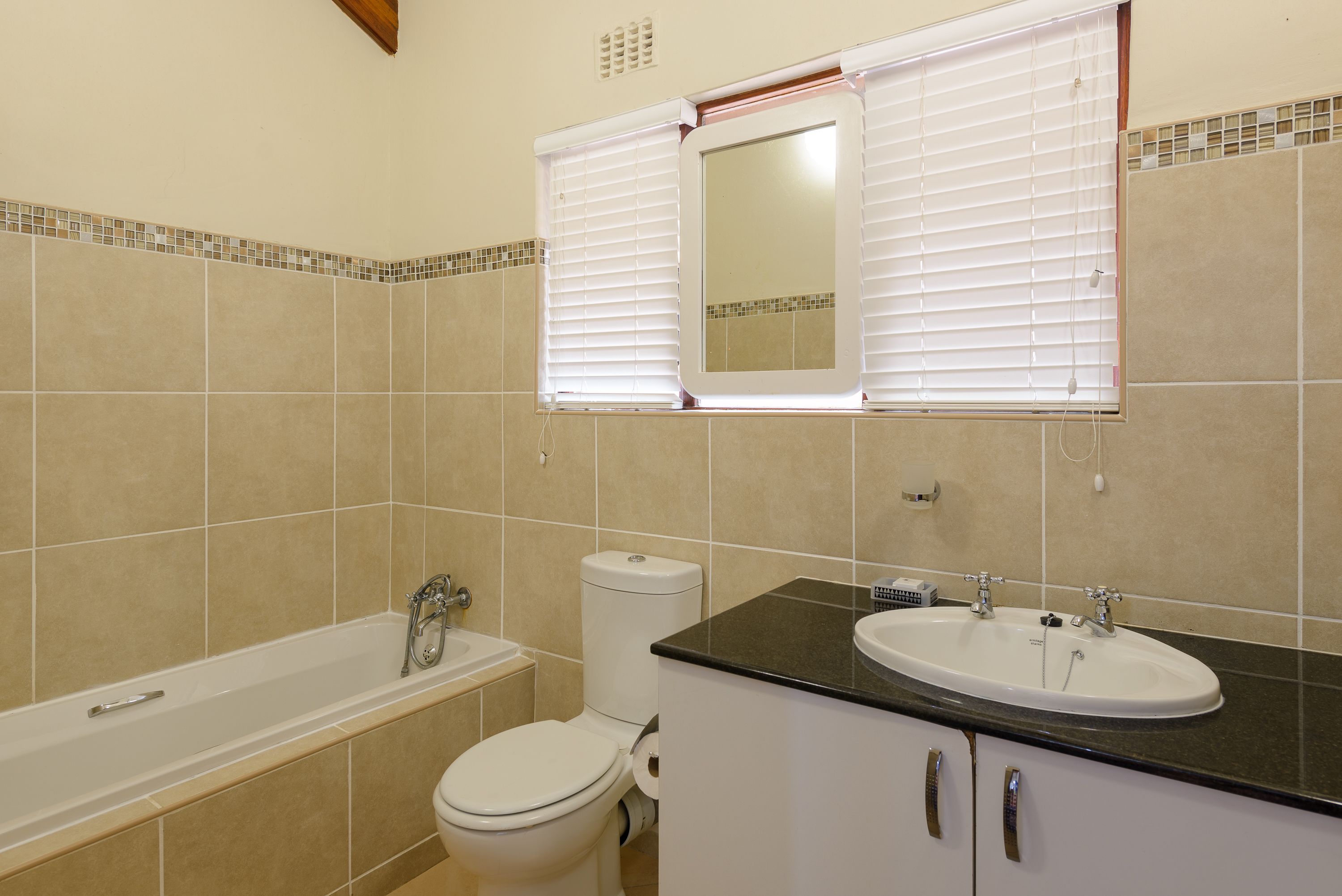 A bathroom with a bathtub, toilet, sink, and a mirror above the sink.