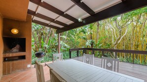 Une terrasse extérieure avec une table et des chaises, un barbecue et une vue sur une végétation tropicale luxuriante.