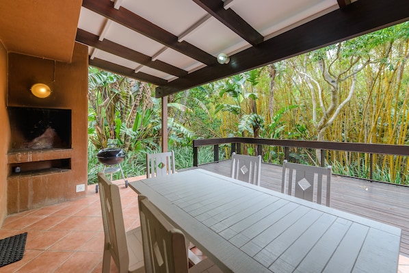 An outdoor patio with a table and chairs, a grill, and a view of dense tropical foliage.