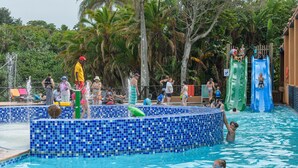 Une piscine dont le bord est recouvert de carrelage, entourée de palmiers et délimitée par une clôture en bois.