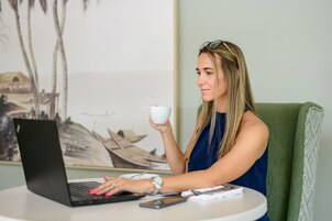 Una persona sentada a una mesa redonda con una computadora portátil, un teléfono inteligente y una taza.