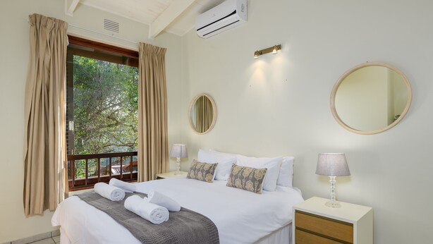 A hotel room with a bed, a nightstand, a mirror, and a window with curtains. - San Lameer Villa Rentals  3014 (Southbroom)