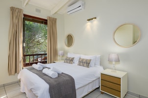 Una habitación de hotel con cama, mesita de noche, espejo y ventana con cortinas.