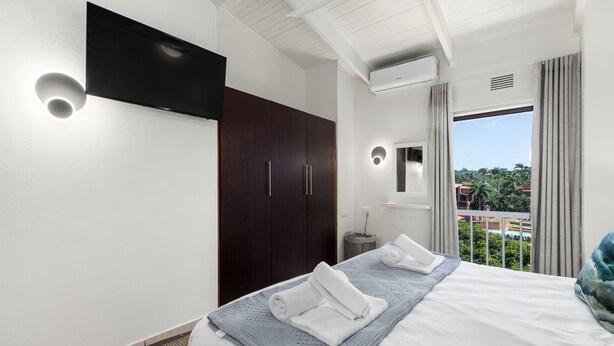 Una habitación de hotel moderna con una cama grande, un televisor de pantalla plana montado en la pared, un armario y un balcón con vistas a la ciudad.