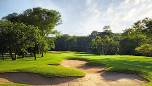 Un campo de golf con búnkeres de arena, árboles y un cielo despejado.