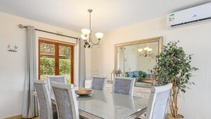 A dining area with a glass table, wicker chairs, a chandelier, a large mirror, and a potted plant. - San Lameer Villa Rentals 2536 (Southbroom)
