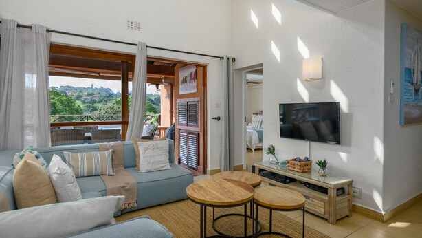 A living room with a sofa, a TV, and a balcony with a view of greenery. - San Lameer Villa Rentals 2536 (Southbroom)
