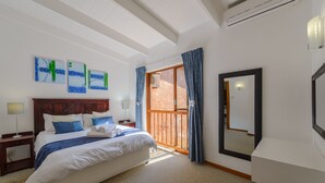 Une chambre à coucher avec un lit, une table de chevet, un miroir et une vue sur l’extérieur.