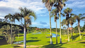 Un campo de golf con palmeras, obstáculos de agua y un club de campo al fondo.