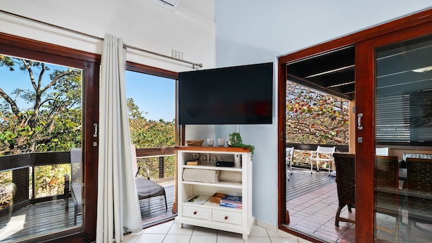 A modern living room with a flat-screen TV, a white console table, and a sliding glass door leading to an outdoor deck. - San Lameer Villa Rentals  2845 (Southbroom)