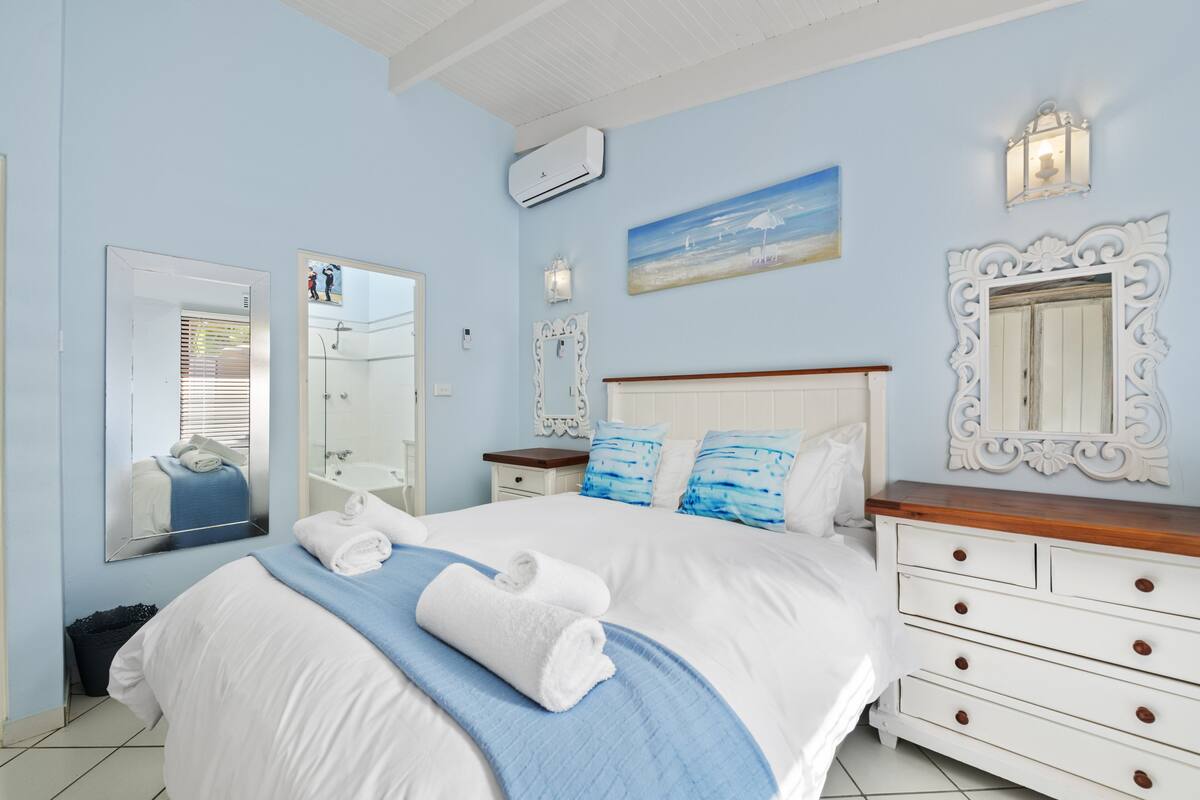 A bedroom with a large bed, a dresser, a mirror, and a painting on the wall.
