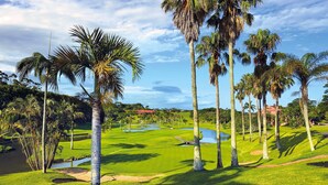 A golf course with palm trees, water hazards, and a clubhouse in the background. - San Lameer Villa Rentals  2845 (Southbroom)