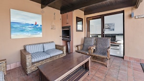 A patio area with a wicker sofa, two chairs, a wooden table, and a pizza oven. - San Lameer Villa Rentals  2845 (Southbroom)