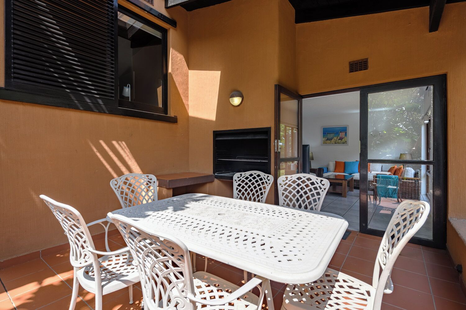 An outdoor patio with a white table and chairs, a TV mounted on the wall, and a sliding glass door leading to an interior space.