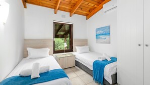 A bedroom with two beds, wooden ceiling beams, a window with a view, and a painting on the wall. - San Lameer Villa Rentals 3116 (Southbroom)