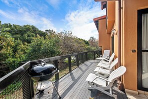 A deck with a grill, white lounge chairs, and a view of dense foliage.