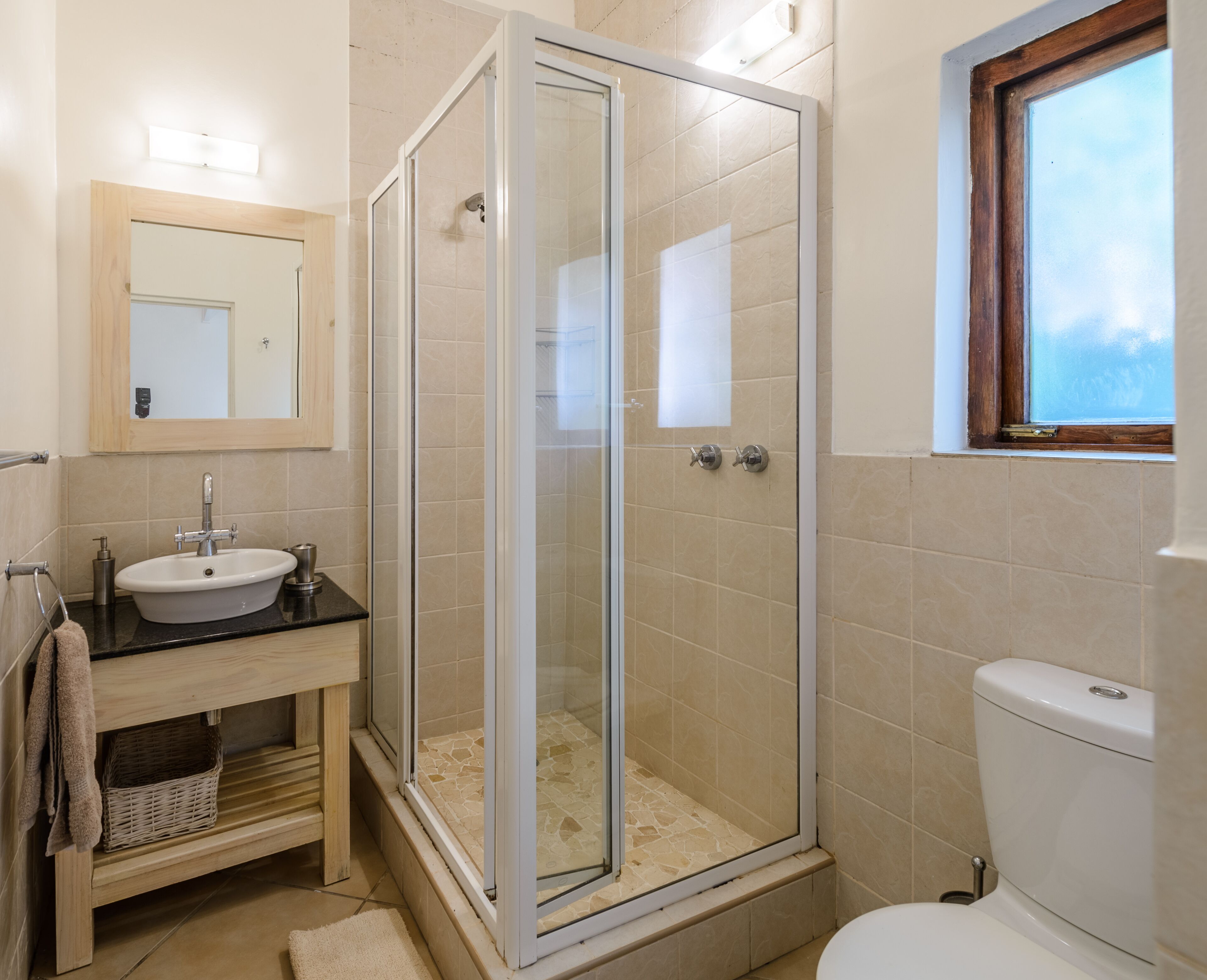 A bathroom with a glass-enclosed shower, a sink with a mirror above it, and a toilet.
