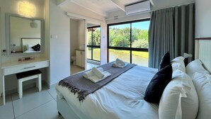 A hotel room with a bed, a desk, a mirror, and a window with a view of greenery. - San Lameer Villa Rentals 3511 (Southbroom)