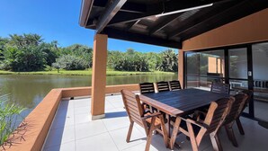 A covered patio with a wooden table and chairs, overlooking a body of water and greenery. - San Lameer Villa Rentals 3511 (Southbroom)