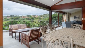 A spacious balcony with a wooden table and chairs, a sofa, and a view of a lush landscape. - San Lameer Villa Rentals 13937 (Southbroom)