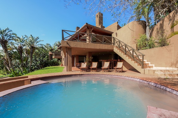 A poolside area with a clear view of a pool, lounge chairs, and a staircase leading to a covered deck.
