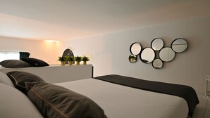 Een moderne slaapkamer met een groot bed, een nachtkastje met planten en een wandspiegel.