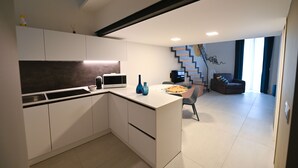 Een moderne keuken met witte kasten, een ingebouwde magnetron en een eethoek met een stoel en tafel.