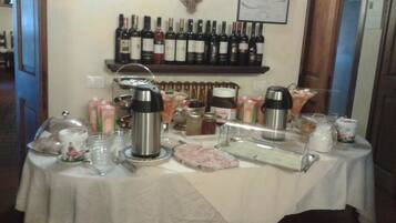 A breakfast setup with a table covered in a white tablecloth, featuring a coffee station, a fruit platter, and a selection of beverages.