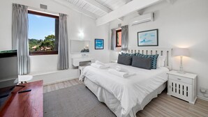 Une chambre à coucher avec un grand lit, des tables de chevet, un bureau et une fenêtre avec des rideaux.