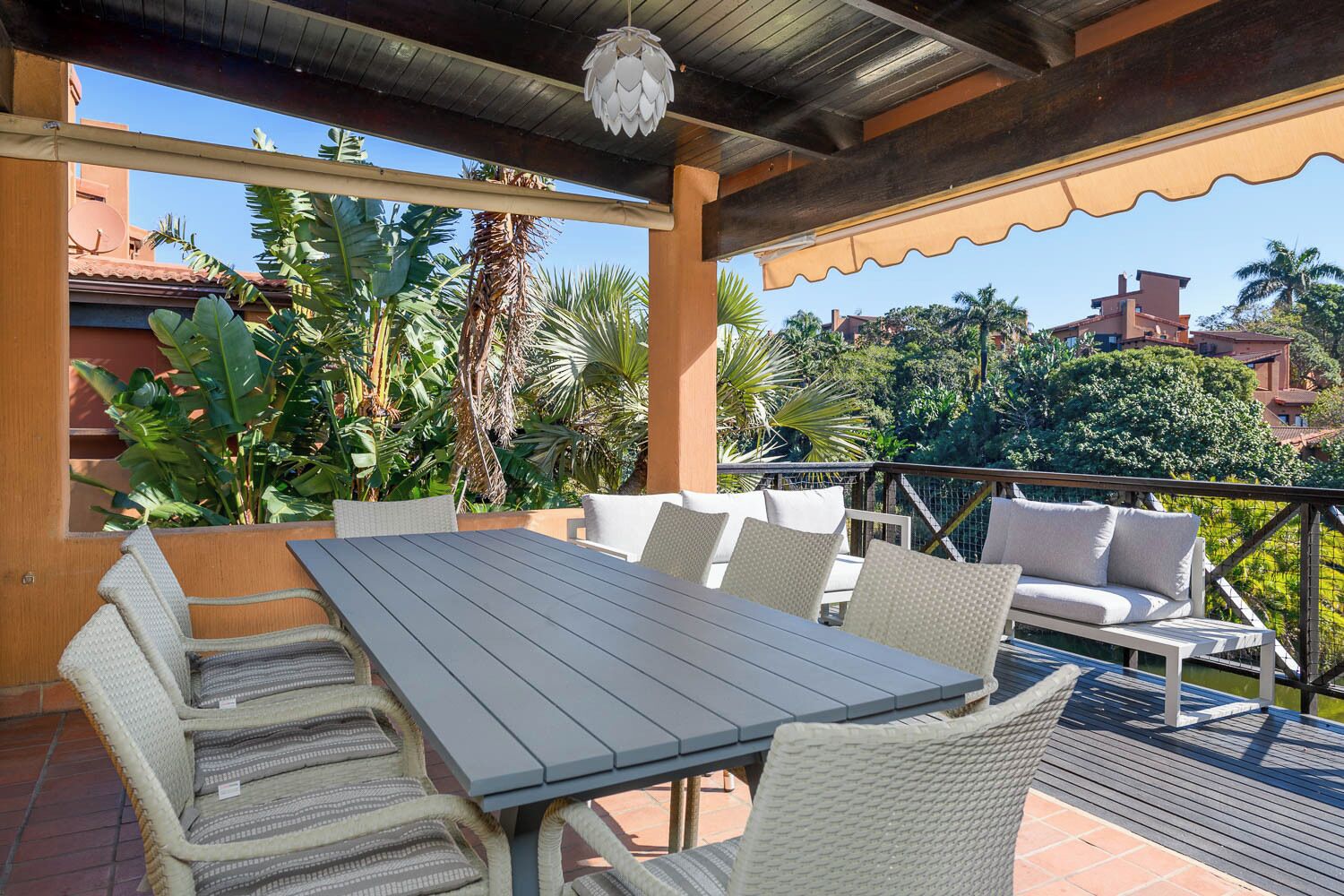 A covered outdoor patio with a table and chairs, surrounded by lush tropical plants.