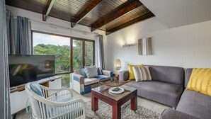 Uma sala de estar moderna com televisão de tela plana, um sofá, uma poltrona e uma mesa de centro.
