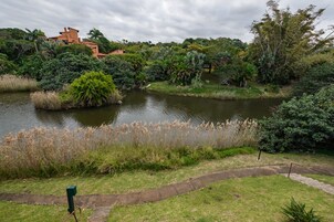 Um rio com uma ponte, cercado por vegetação exuberante e um edifício ao fundo.