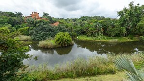 A serene pond surrounded by lush greenery and a few buildings in the background. - San Lameer Villa Rentals 3108 (Southbroom)