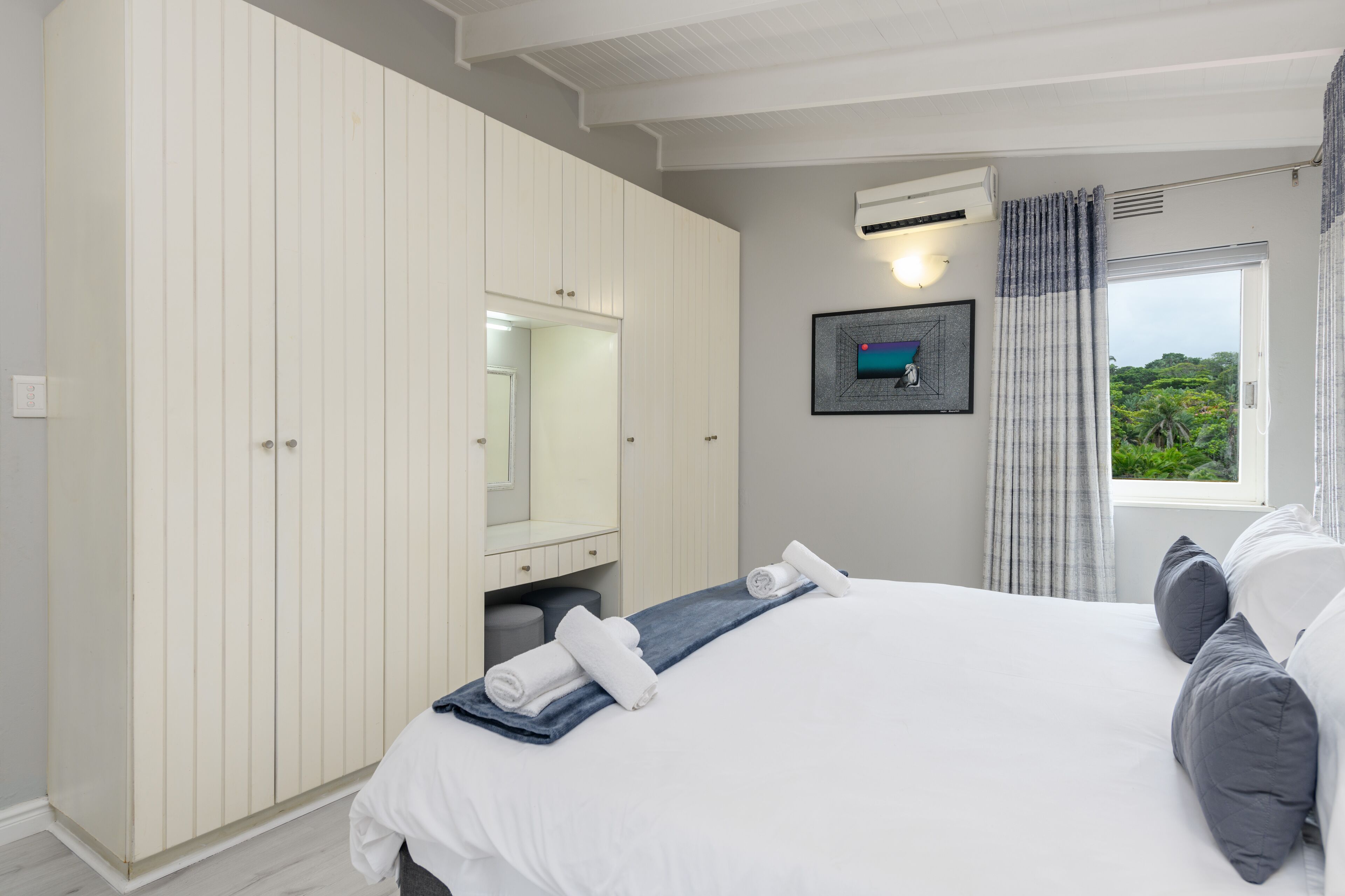 Une chambre à coucher avec un grand lit, une armoire, un miroir et une fenêtre avec des rideaux.