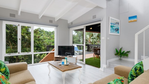 A modern living room with a TV, sofa, and coffee table. There are large windows and a view of greenery outside. - San Lameer Villa Rentals 3108 (Southbroom)