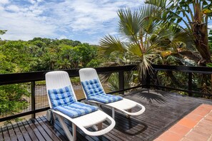 A wooden deck with two white lounge chairs with blue cushions, surrounded by lush greenery and a clear sky. - San Lameer Villa Rentals 3108 (Southbroom)