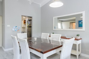 A dining area with a rectangular table, white wicker chairs, a wooden sideboard, and a large mirror on the wall. - San Lameer Villa Rentals 3108 (Southbroom)