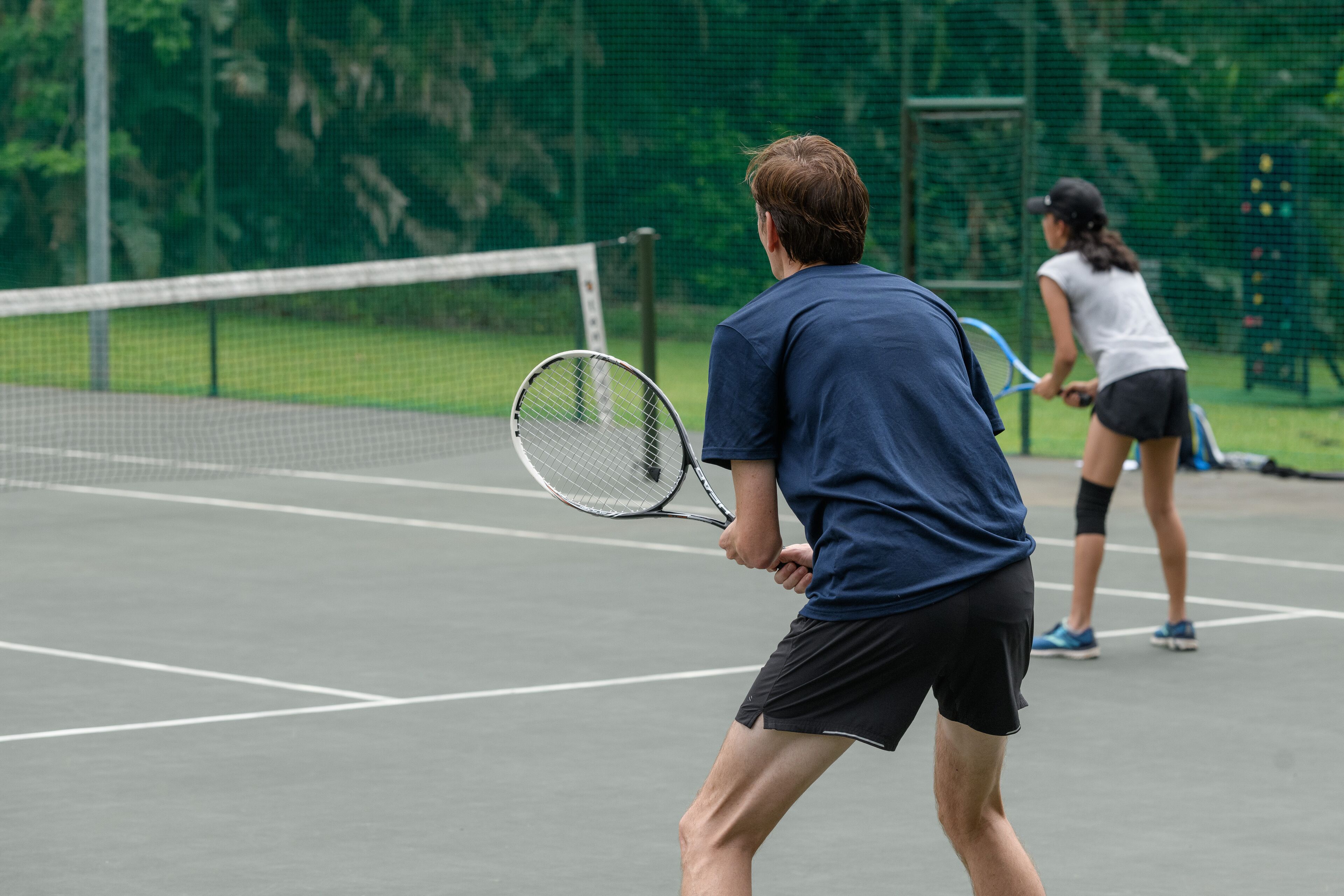 Ein Tennisplatz mit Netz in der Mitte, umgeben von einem grünen Zaun.