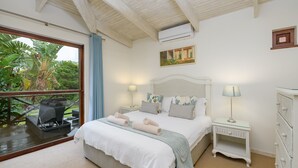 A bedroom with a large bed, two bedside tables with lamps, a window with a view of greenery, and a ceiling fan. - San Lameer Villa Rentals 2702 (Southbroom)