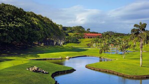 A golf course with a pond, lush greenery, and a building with a red roof. - San Lameer Villa Rentals 2702 (Southbroom)