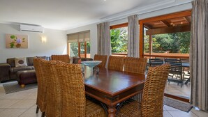 A dining area with a wooden table and wicker chairs, a sofa, and a view of the outdoors through large windows. - San Lameer Villa Rentals 3011 (Southbroom)