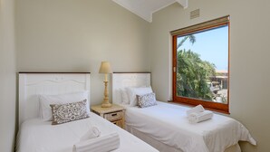 A hotel room with two beds, a nightstand with a lamp, and a window with a view of palm trees. - San Lameer Villa Rentals 3011 (Southbroom)