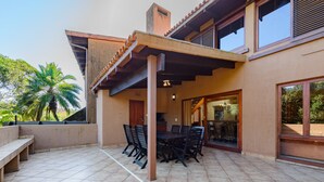 A covered patio with a dining table and chairs, a staircase leading to an upper level, and a view of palm trees. - San Lameer Villa Rentals 3011 (Southbroom)