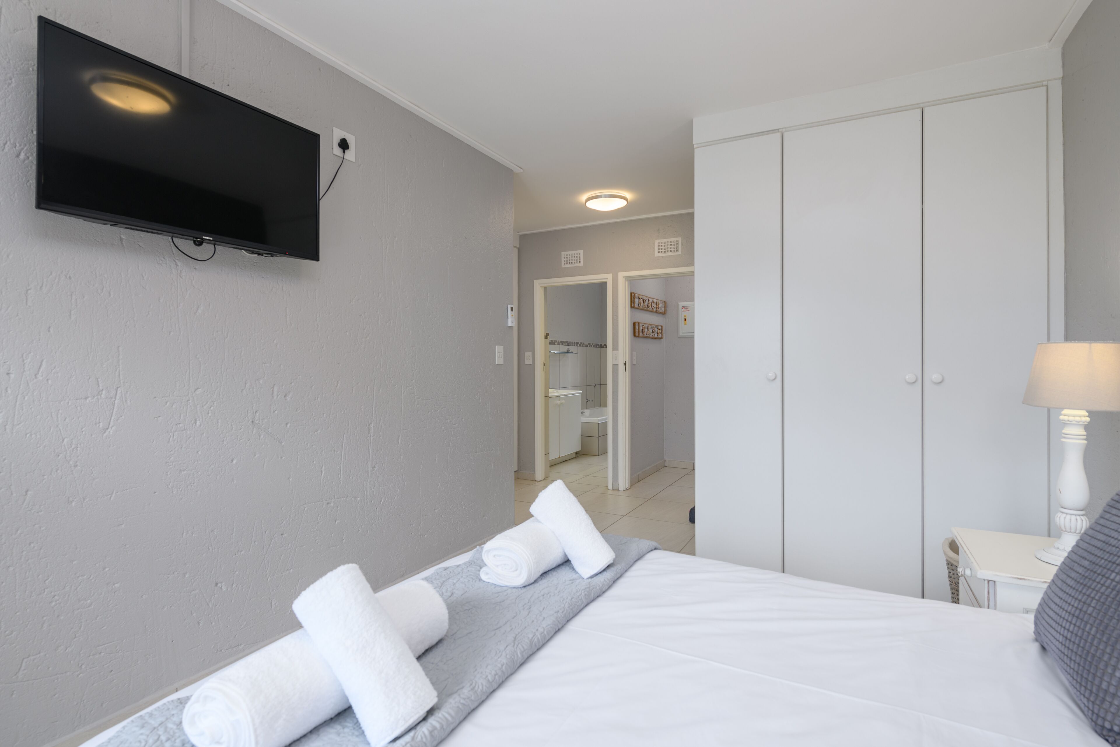 A hotel room with a bed, a flat-screen TV mounted on the wall, a bedside table with a lamp, and a wardrobe.