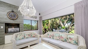 A modern living room with wicker furniture, a built-in grill, and a large window overlooking greenery. - San Lameer Villa Rentals 3708 (Southbroom)