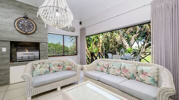 A modern living room with wicker furniture, a built-in grill, and a large window overlooking greenery.