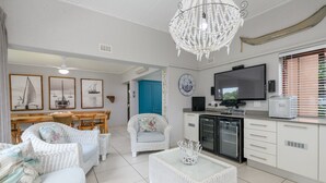 A modern living room with white wicker furniture, a chandelier, and framed nautical paintings. - San Lameer Villa Rentals 3708 (Southbroom)