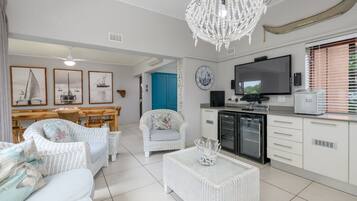 A modern living room with white wicker furniture, a chandelier, and framed nautical paintings.