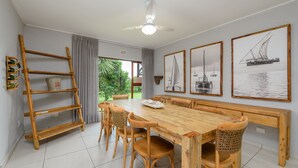 A dining area with a wooden table and chairs, a ceiling fan, and framed maritime paintings on the wall. - San Lameer Villa Rentals 3708 (Southbroom)